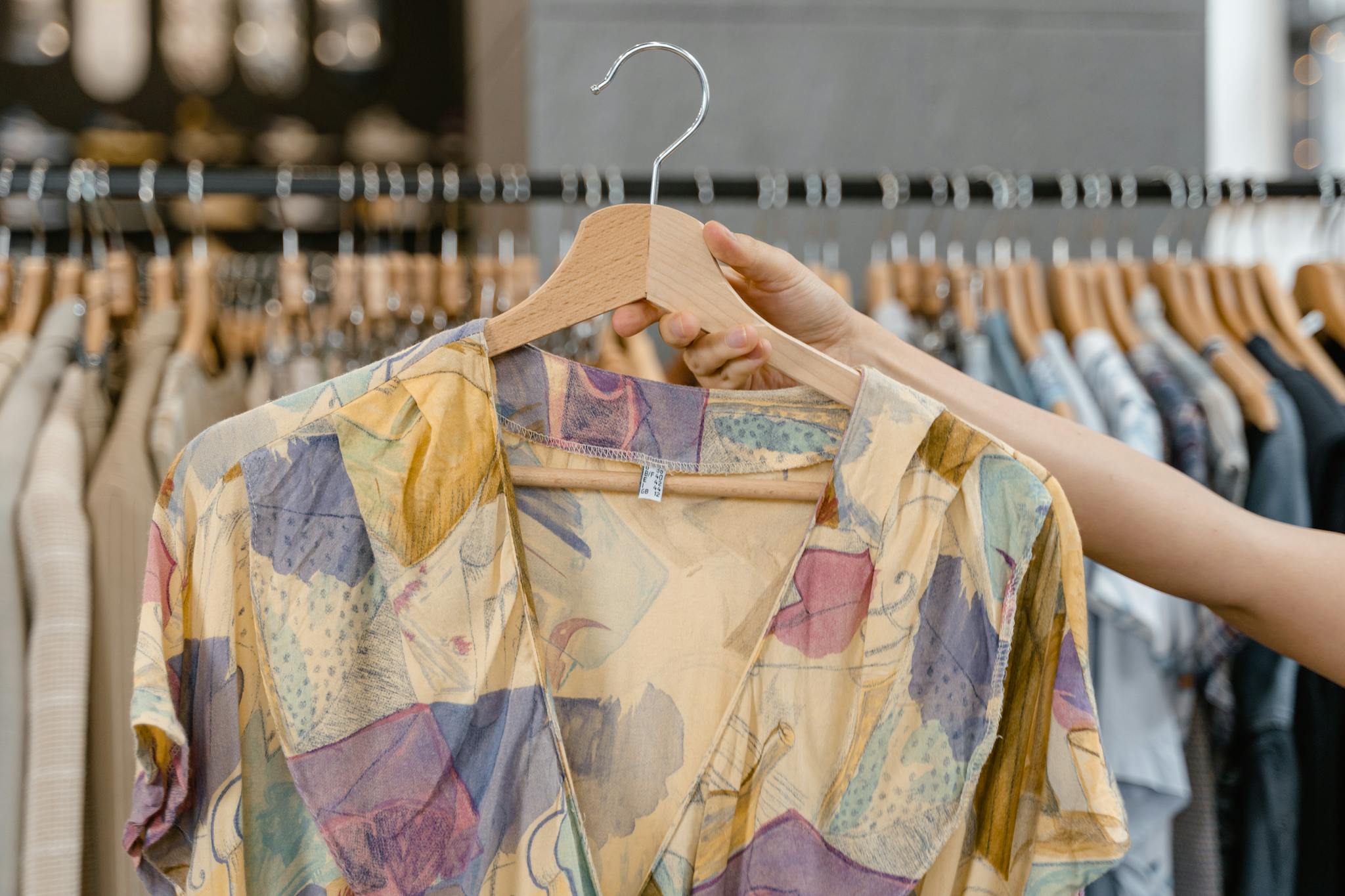 About A person holding a vibrant patterned dress on a hanger inside a clothing store.