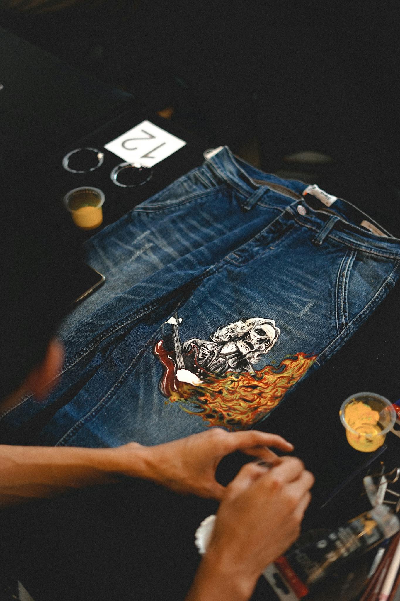 Home Close-up of artist painting a unique design on blue denim jeans with vibrant colors.