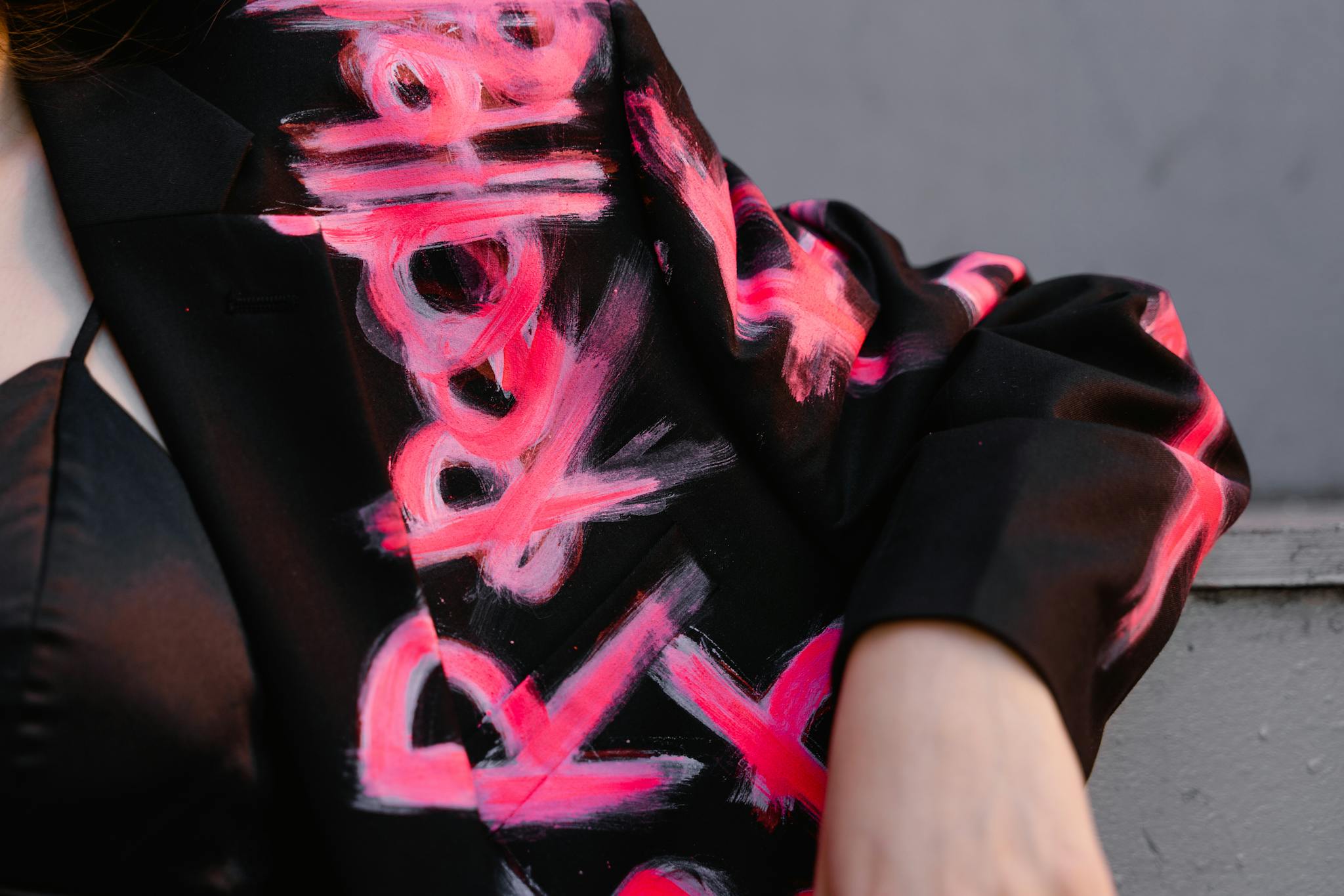 About Detailed close-up of a black blazer with vibrant hand-painted abstract art design in pink.