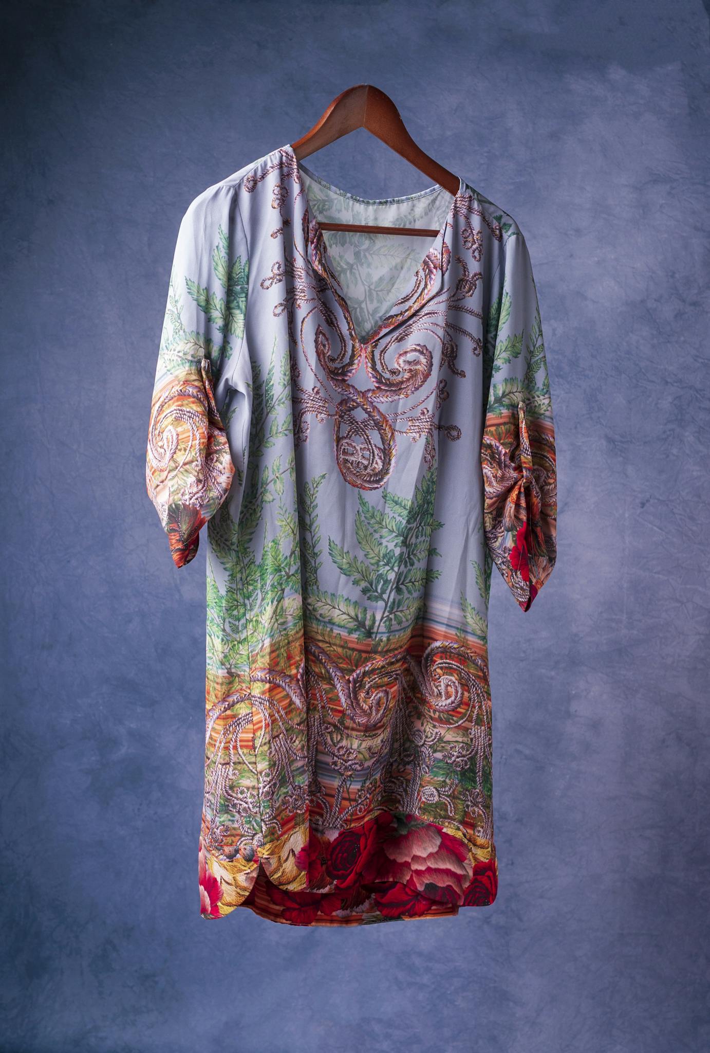 Home Stylish elegant dress with intricate patterns hanging on a wooden hanger in a studio setting.